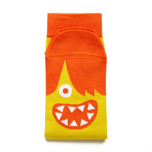Folded yellow socks have orange trim at the top and the toes. A face appears below the toes with orange hair covering one eye, and an open smile with triangular teeth. 