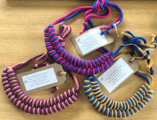 3 fabric necklaces with different colours. Colours overlap so the design appears striped. Each necklace has a card tag attached with string. 