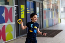 Load image into Gallery viewer, Child laughs to someone off camera. He is wearing a dark blue shirt with satellite shapes and blue jeans. 
