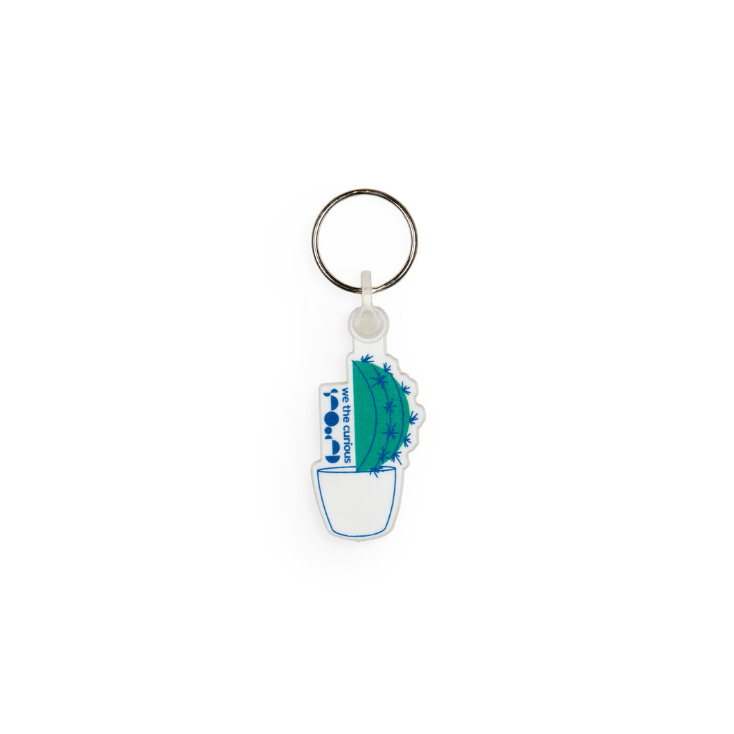Keyring design shows green cactus in a white pot, with We The Curious logo to the side of the cactus. 
