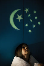 Load image into Gallery viewer, Stars are stuck to a wall and glowing while a young girl sits underneath. 
