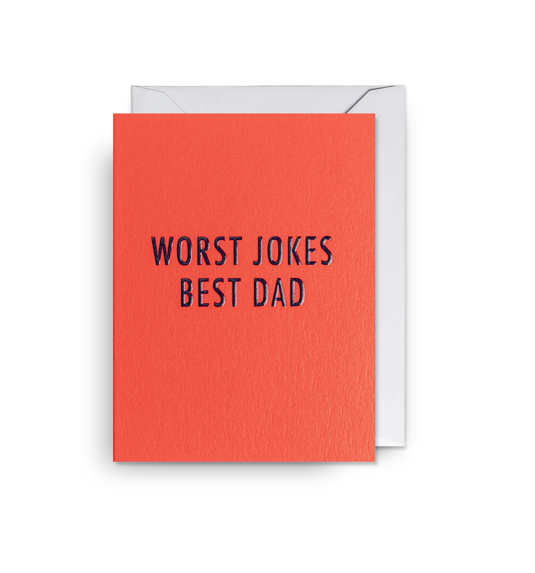 Red-orange card with black letters reading 'worst jokes best dad' in all capitals. White envelope tucked in. 