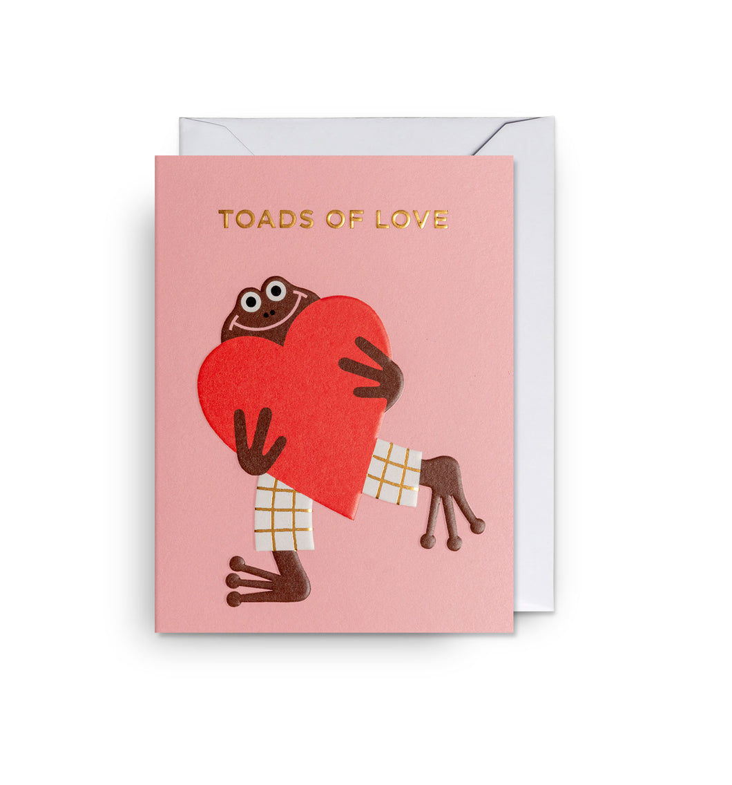 Pink card with gold lettering. Brown smiling toad holds a red heart and wears checkered trousers.