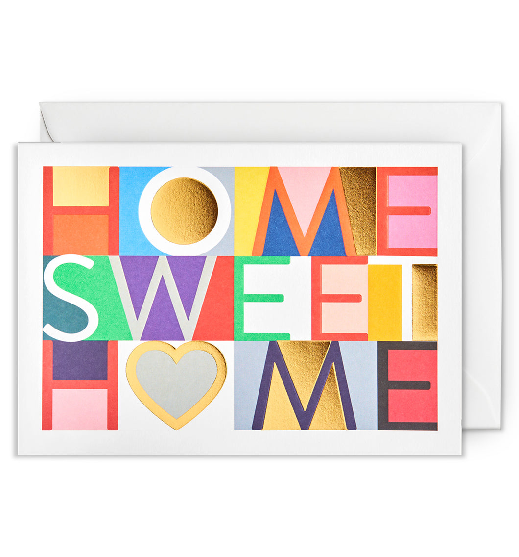 White card with colourful squares and letters reading 'home sweet home'. white envelope tucked behind. 