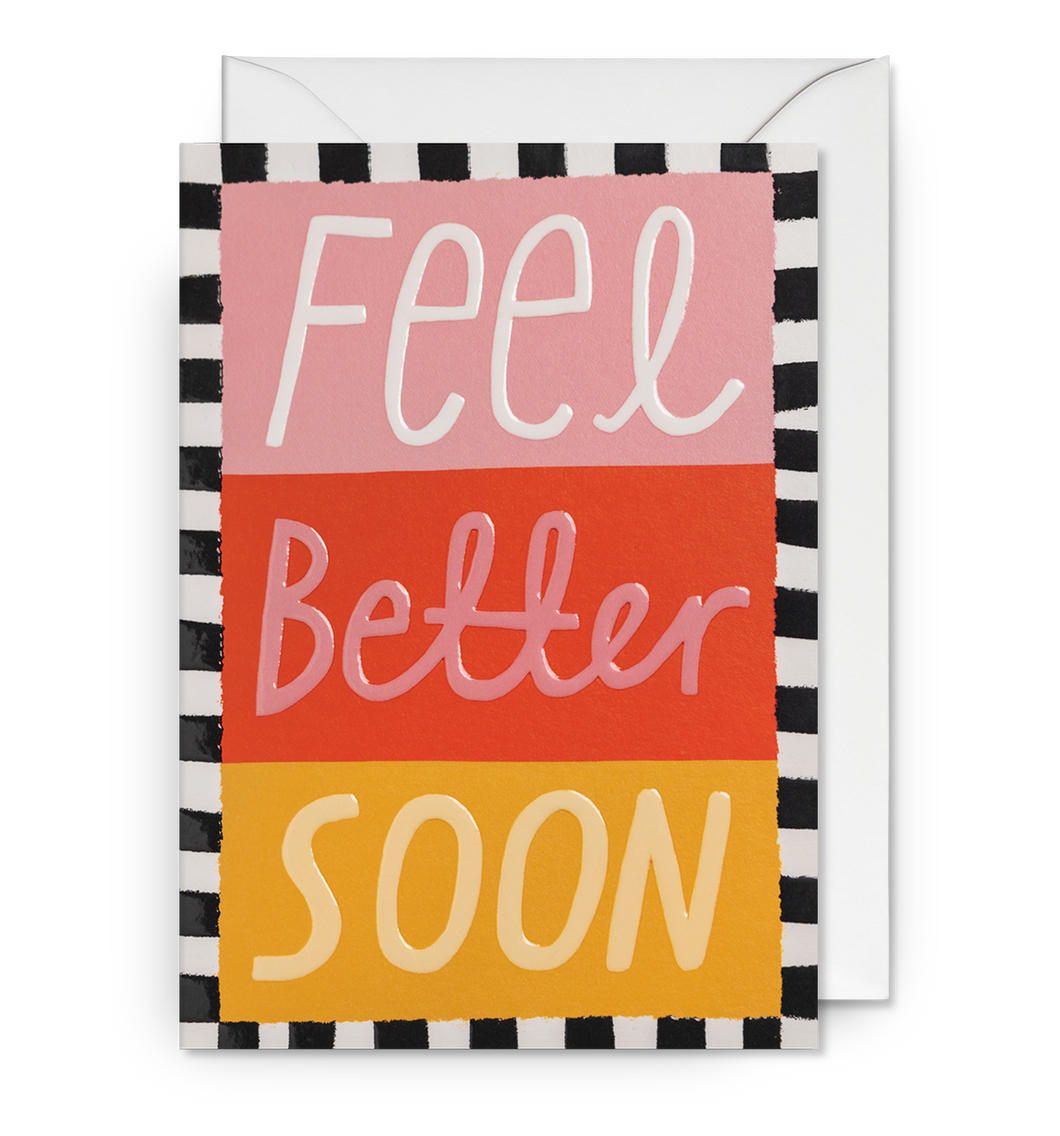 Pink, red and yellow card with black and white border. Large letters read 'feel better soon'. Card sits on white envelope.