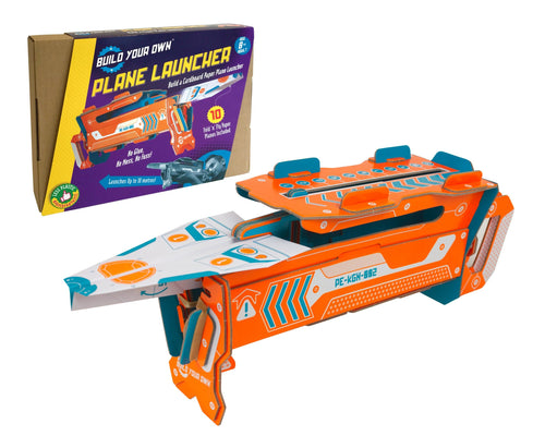 Orange and blue cardboard plane launcher built in front of the cardboard box. Plane launcher holds a paper airplane. 
