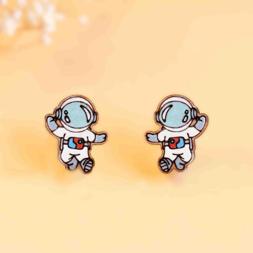Two earrings are painted and cut to look like astronauts with the visors down. They are asymmetrical, and waving with different arms. 