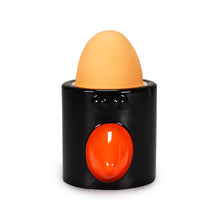 Load image into Gallery viewer, Black egg cup with black eyes and orange beak. Egg sits inside. 
