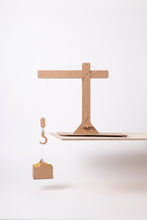 Load image into Gallery viewer, Crane sits on the end of a wooden board. The crane holds a small box filled with dried pasta. 
