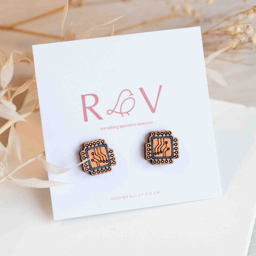 Two wooden earrings in square shape with computer chip design painted in orange and blue attached to a white card. Card reads 