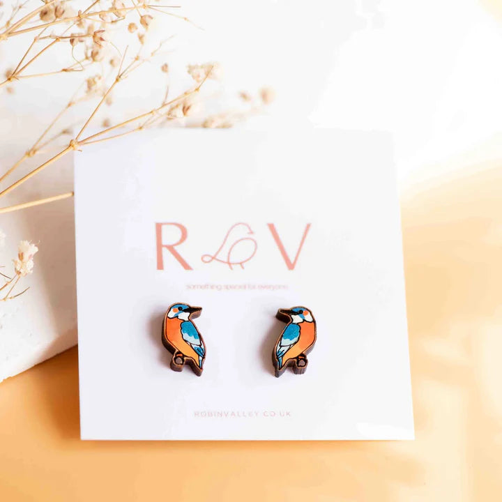 Orange & blue bird-shaped earrings on a card with set against a neutral background.