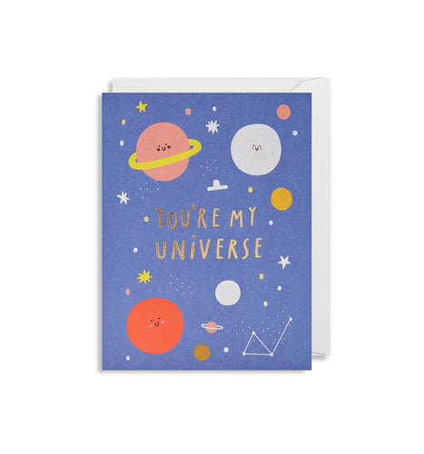 Blue card with white envelope tucked inside. Colourful illustrations of smiley-faced planets, stars, and constellations. In gold-foiled capital letters, the card reads 'you're my universe'.