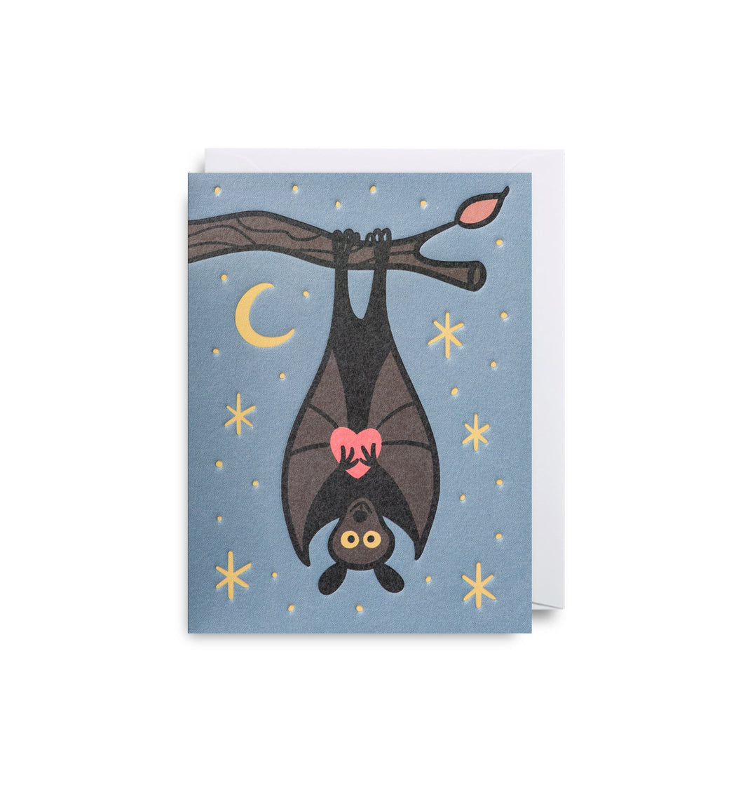 Blue card shows a bat hanging upside down from a branch clutching a pink heart. the background has stars and a moon. A white envelope is tucked into the card.
