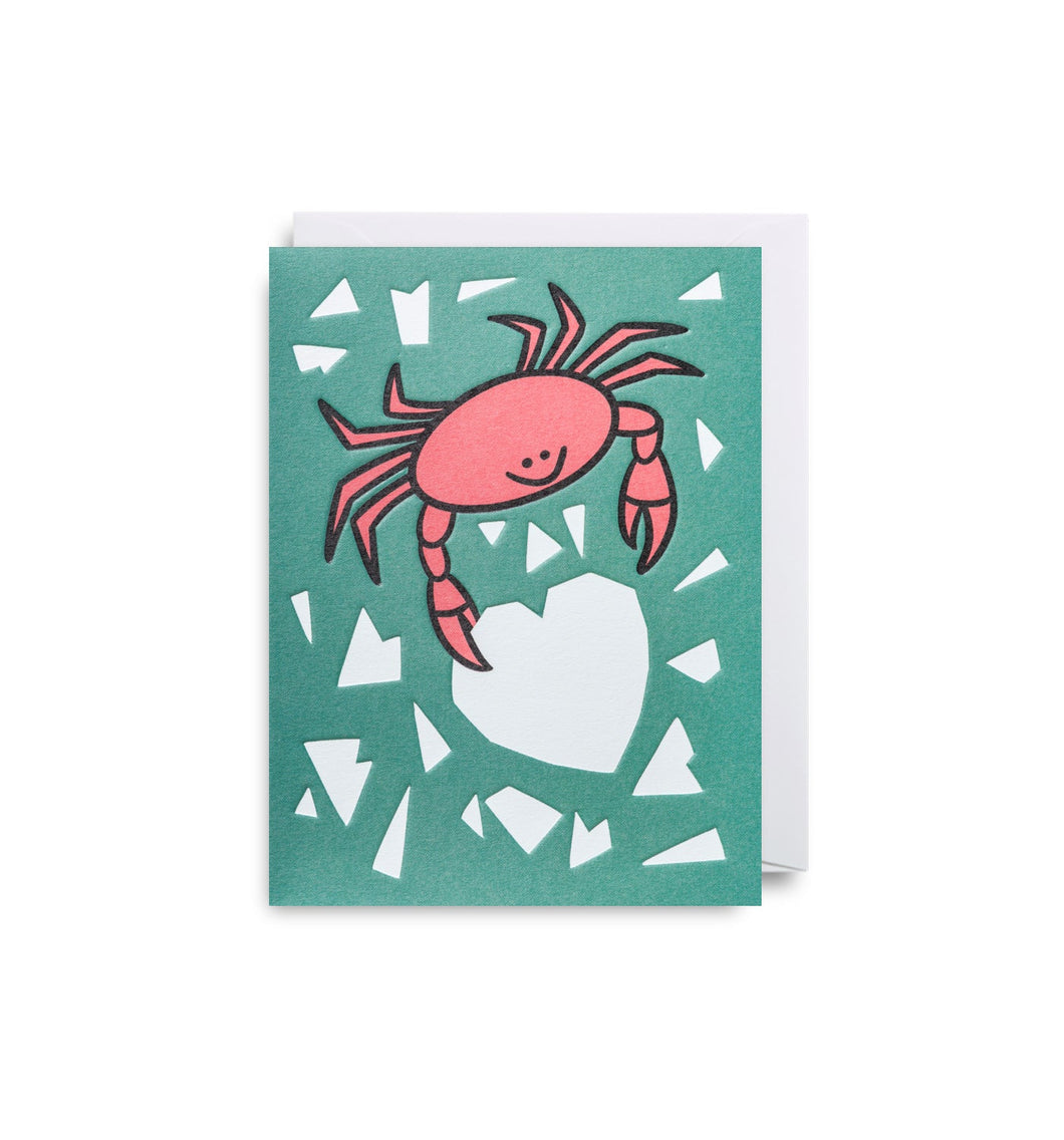 Green card with red crab cutting a white heart out of paper. White envelope.
