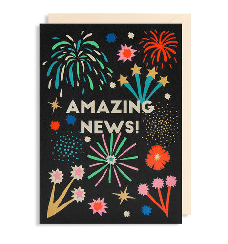 Black card with cream envelope tucked in. Full-colour illustrations of different types of fireworks. In the middle in white capital letters, the card reads 'Amazing news!'