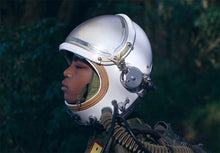 Load image into Gallery viewer, A colour photograph of a black child wearing a helmet with tubes connecting to a backpack. 
