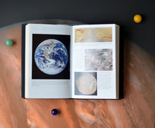 Load image into Gallery viewer, Open book and three balls (yellow, green and blue) rests on image of Jupiter. 4 photos on the page with captions. Photo on the left is of Earth, then images on the right have close ups of texture.

