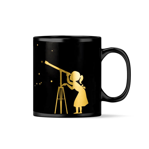 Black mug with handle to the right. In gold theshadow of a child with a dress and ponytail looking through a telescope at some dots (representing stars). 