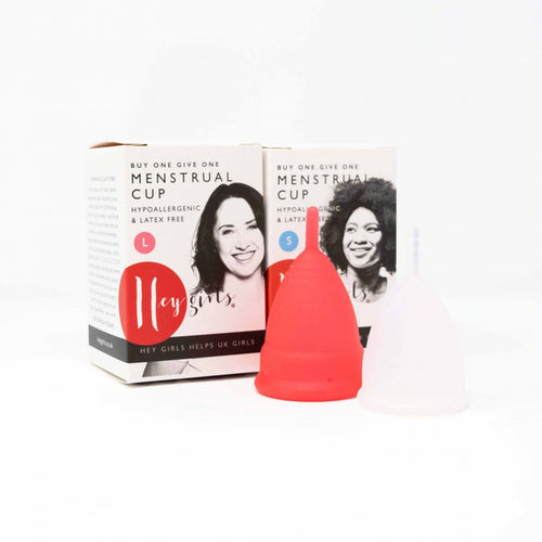 Red and white menstrual cups sit in front of two cardboard boxes. Boxes have small symbols for size. Large box shows a smiling white woman, small box shows smiling Black woman. Boxes both read 'buy one give one menstrual cup, hypoallergenic and latex free'. 