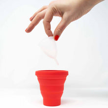 Load image into Gallery viewer, Light-skinned hand lowers a clean menstrual cup into the red pot.
