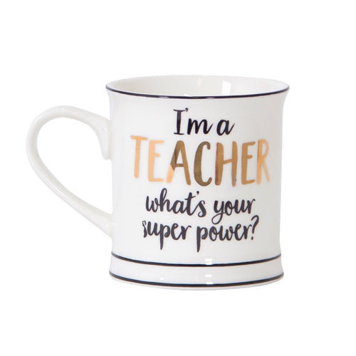 White mug with black trim reads 'I'm a teacher, what's your superpower?'. Teacher is written in gold foil, and the rest of the letters in black cursive.