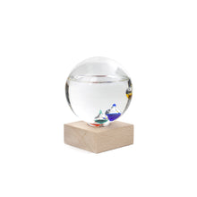 Load image into Gallery viewer, Glass Galileo Thermometer is a globe rests on square wooden block. Smaller globes inside are multi-coloured (yellow, blue, teal, red can be seen) and floating at different heights. Liquid in the globe is three quarters full.
