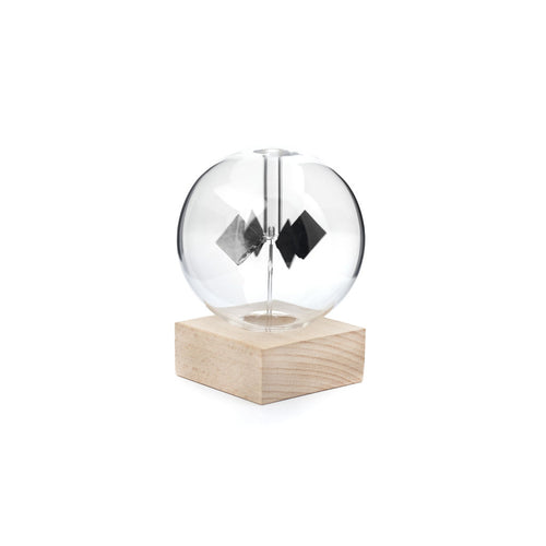 Solar radiometer is glass globe with black rotating squares inside. Rests inside wooden square block for base. 
