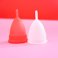 Load image into Gallery viewer, Close up of two menstrual cups. Large cup is red, smaller cup is translucent white. 
