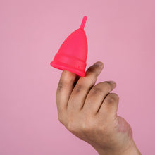 Load image into Gallery viewer, Black hand holds a clean red menstrual cup. 
