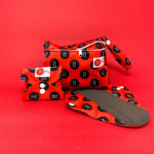 Load image into Gallery viewer, Red bag with black dots, a folded and buttoned period pad and an open one with grey liner. 
