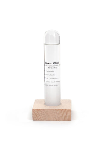 Storm glass is a tube resting inside a square wooden block. Storm glass has details listed on the outside to assist with understanding contents. 