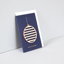 Load image into Gallery viewer, Blue portrait card with wooden ornament attached and white envelope inside. Card reads &#39;Season&#39;s Greetings&#39; across the bottom in small gold letters. Ornament is attached and has a string for hanging. Ornament is round and striped. 
