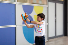 Load image into Gallery viewer, 7-8 year old light-skinned boy holds an orange and blue seacopter in both arms beside his body. He is wearing a white t-shirt with colourful shapes and blue jeans. 
