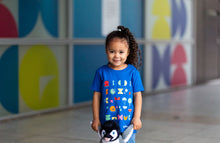 Load image into Gallery viewer, Child is wearing a blue top with colourful shapes and a pair of jeans. 
