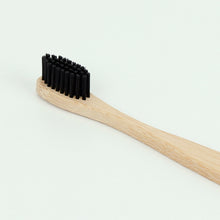 Load image into Gallery viewer, Close up on the black bristles of the toothbrush also shows the wood grain of the handle. 
