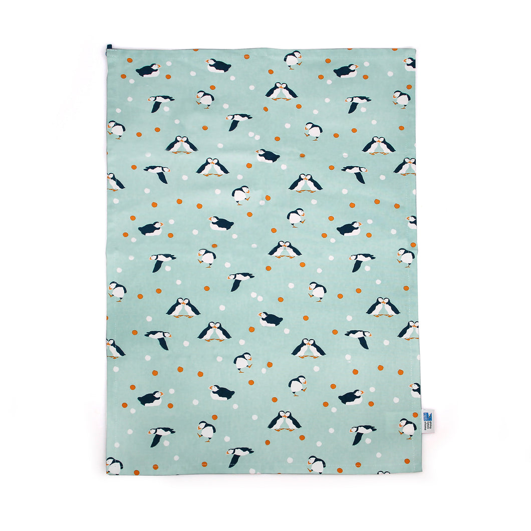 Light blue grey tea towel with puffins in various poses (flying, standing with one foot out, touching noses with another, lying flat down), and orange and white dots.