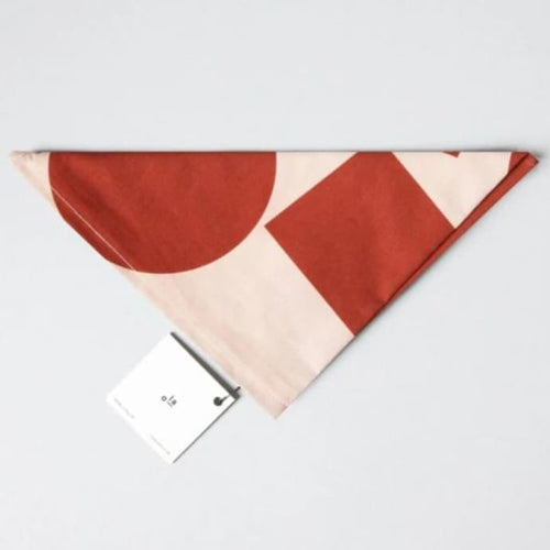Wrap is folded into a neat triangle. The wrap is an off-white, with red-orange circles and squares. A square card tag is attached with a metal safety pin.