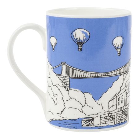 Mug has white handle, blue background with white illustration of Clifton Suspension Bridge, hot air balloons. River and sky are the blue background.