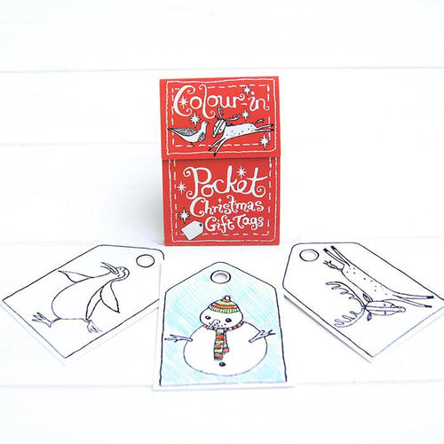 Three tags spread in front of red packaging. Cards show a penguin, snowman and a reindeer. Packaging reads 'colour-in pocket Chrismas gift tags'. 