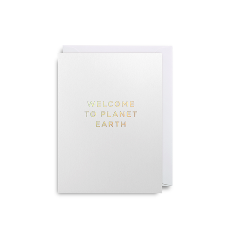 Silver card with white envelope tucked inside. Gold foil capital letters read 'welcome to planet earth'.