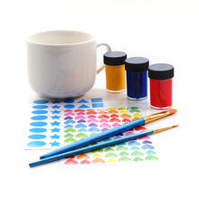 Load image into Gallery viewer, Contents of box spread out, 1 white mug, 3 pots of paint (yellow, blue and red), 2 brushes of varying size, and 2 sticker sheets with differently coloured hearts and blue shapes (2 circle sizes, stars, triangles, squares)
