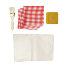 Load image into Gallery viewer, Contents of the packaging are laid out flat. There is a wooden brush, 3 red and white folded checked fabric pieces, 1 block of beeswax and parchment paper folded below.
