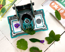 Load image into Gallery viewer, A top down view of the microscope with a leaf under the scope. A flower sits in a specimen tray to the side.
