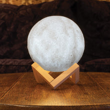 Load image into Gallery viewer, Moon light resting on wooden base on top of a table. Light shown is neutral setting.

