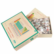 Load image into Gallery viewer, Open puzzle box with lid half on at an angle. Inside the box is a plastic bag filled with puzzle pieces and a poster sticks out with puzzle image.
