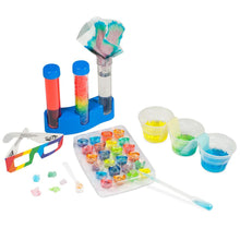 Load image into Gallery viewer, Box contents laid out mid activity. A tray of 24 plastic cups with different coloured substances. 3 plastic cups with yellow, green and blue liquids connected with 2 cloths dipped in 2 containers each. 3 test tubes sit on a blue stand. One filled with red liquid, 1 filled with rainbow layers of crystals, one with clear substance and tie-dyed cloth inside. Rainbow glasses in bottom left. Pipette filled with blue liquid.
