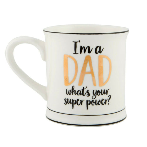 White mug with black trim reads 'I'm a dad, what's your superpower?'. Dad is written in gold foil, and the rest of the letters in black cursive.