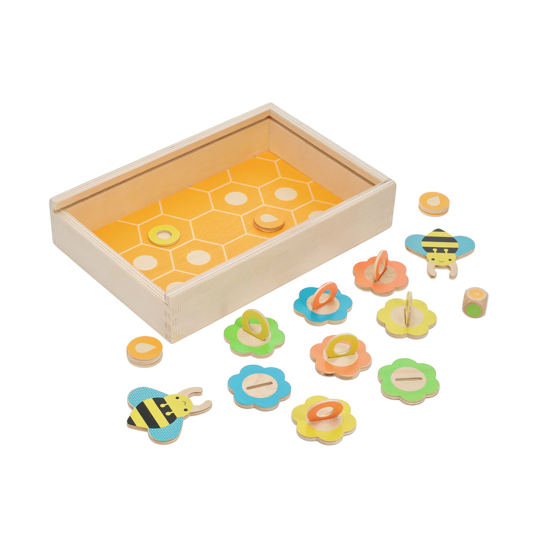 A wooden box with honeycomb shapes on the bottom is surrounded by 8 wooden flowers and 2 bees. There are also two types of circular pieces and a coloured die.