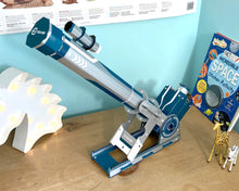 Load image into Gallery viewer, An image of the telescope on a wooden surface with a book and toys for scale.
