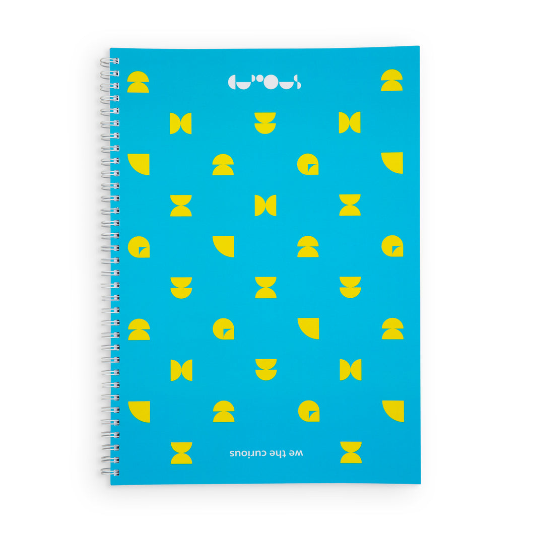 Blue notebook with yellow shapes. Spiral is white. At the top of the notebook, the We The Curious logo is in white. At the bottom of the notebook 